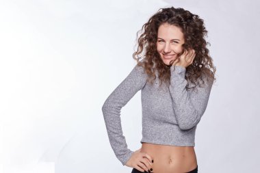 Young female demonstrates flat stomach and slim waist standing on blank studio wall. Woman with beautiful body and playful look having cosmetic treatment in beauty clinic. Health care and medicine.