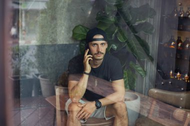 Ciddi doz erkek freelancer sakallı, rahat t gömlek giyer, sportif rahat tarzı vardır, ortak ya da cep telefonu üzerinden iş arkadaşı ile konuşuyor, tatlı ile kahve bekler, sıkı ifade yoğunlaşmıştır.