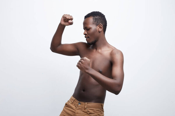 Happy curly haired African American male starts his morning in good mood, doing exercises, sports and dancing. Positive beginning of new day. Shirtless athlete man isolated on white studio background.