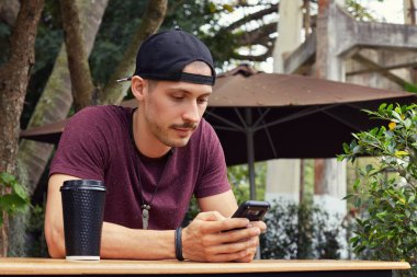 Kahve café'de sınıfları sonra üniversitede iken ciddi ve yoğun yüz ifadesi ile ekrana bakarak yakışıklı Avrupa öğrenci rahat t-shirt ve şapka cep telefonunuzun.
