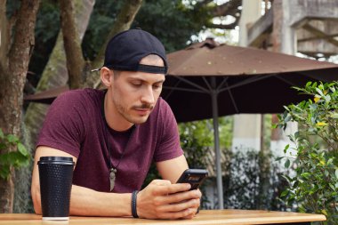 T-shirt ve şapka, ciddi meşgul Avrupa girişimci istimal hareket eden telefon için iş yazışmaları, konsantre bakışla ekrana bakarak portresi. Yüz ifadeleri, duygular kavramı.