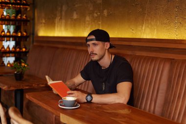 Çekici düşünceli sakallı adam dalgın ifade ile uzak görünüyor, kafeteryada oturur, kitap tutan, bilimsel araştırma, okuma gerekli belgeleri, eğitim ile meşgul için hazırlar. Okuma kavramı.