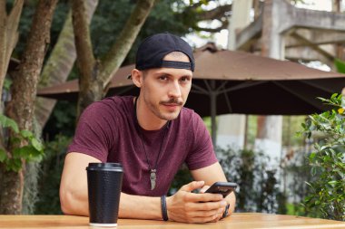 Kentsel peyzaj arka planı arıyorum ve fotoğraf makinesi ile neşeli yüz ifadesi sırasında cep telefonuyla mesaj sokulgan yolu ile sosyal ağlar, gülümseyen sokak aşınmaya yakışıklı adam oturan.