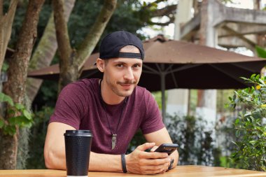 Kentsel peyzaj arka planı arıyorum ve fotoğraf makinesi ile neşeli yüz ifadesi sırasında cep telefonuyla mesaj sokulgan yolu ile sosyal ağlar, gülümseyen sokak aşınmaya yakışıklı adam oturan.