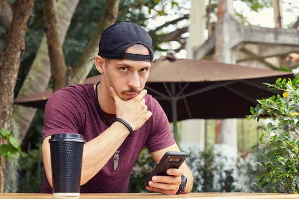 Masada açık havada kupa ve cep telefonu ile el oturan modern café'de sohbet ederken iş bulma yeni yaklaşımlar ve çözümleri üzerinde odaklı çene, dokunmadan düşünceli Kafkas yakışıklı adam.