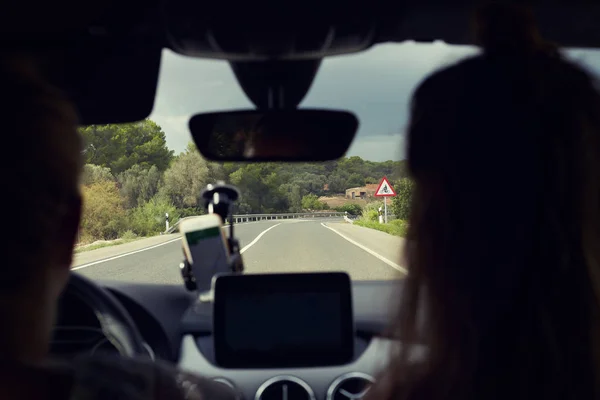 Selective focus on road. Close-up shot two female silhouettes traveling by automobile. Good view of long road with curves and signs. Young driver uses navigation on phone. Mock up for advertising.