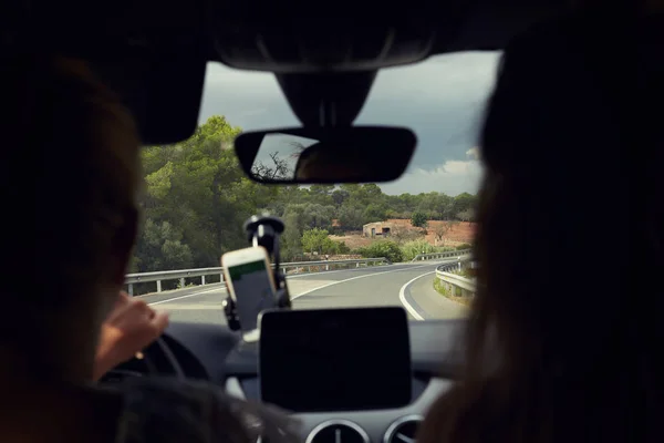 Selective focus on road. Close-up shot two female silhouettes traveling by automobile. Good view of long road with curves and signs. Young driver uses navigation on phone. Mock up for advertising.