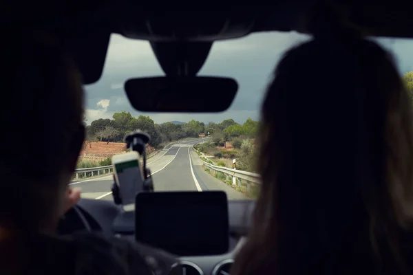 Selective focus on road. Close-up shot two female silhouettes traveling by automobile. Good view of long road with curves and signs. Young driver uses navigation on phone. Mock up for advertising.