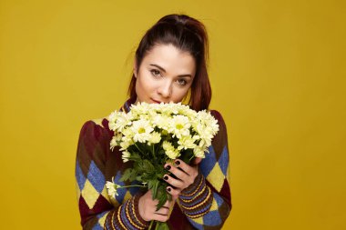 Çiçekler iki eliyle şefkatle tutarak, derin, karanlık gözler, sarı arka plan üzerinde izole kameraya bakarak karışık yarış kartlarının genç ve kadın ile kırmızı parlak saçlar temiz cilt, yatay atış yukarıya kapatmak