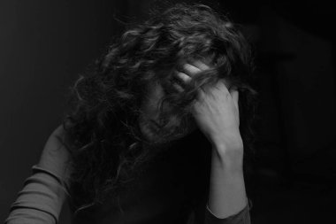 Siyah ve beyaz otantik yatay portre düşünceli tanınmayan kıvırcık saçlı kadın modeli, kafasına el tutarak, gizemli bir şekilde gizleme yüz, karanlık oda kapalı poz. Güzellik konsepti.