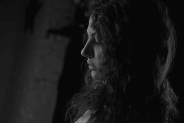 Genç kadın profilinin otantik siyah ve beyaz yatay portre, karanlık odada ayakta. Kıvırcık saçlı şehvetli beyaz kadın, kapalı poz ayrıntılı çekim yakın. Gençlik ve güzellik konsepti.