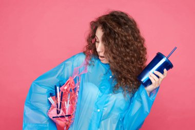 Kıvırcık saçlı, şaşırmış yüz ifadesi ile şaşıran kadın, tüm şık ve modaya uygun giysileri polietilen ve geri dönüşüm malzemesi nden yapılmış olduğunu fark etti. Çevre koruma kavramı.