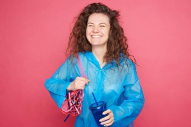 Yakın kamera gülerek kıvırcık saçlı kadın, dünya temizlik gurur ve mutluluk gösterir, geri dönüşümlü plastik şeyler tutar, pembe arka plan karşı duruyor. İnsanlar, çevre, kirlilik