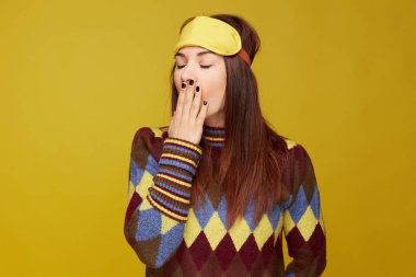 Uykulu karışık yarışçı kadın geniş açık ağız ile esneme Closeup portre, gözleri kapatarak, alnına uyku maskesi giyen, sarı duvar arka plan üzerinde poz. Yüz ifadesi, vücut dili kavramı.