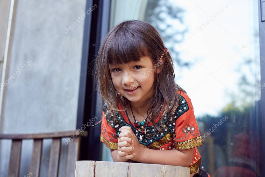  Authentic portrait of pretty thai baby girl posing outdoors, dressed in traditional colorful dress, jewelry, being in good mood,smiling and looking at camera. Attractive child enjoying life