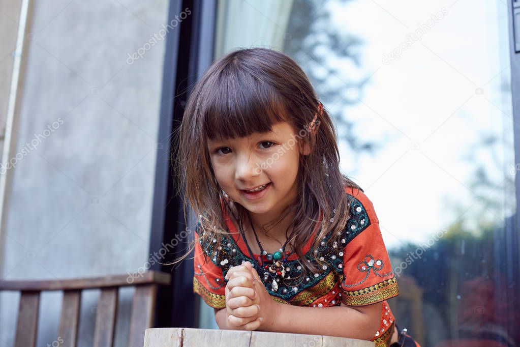  Authentic portrait of pretty thai baby girl posing outdoors, dressed in traditional colorful dress, jewelry, being in good mood,smiling and looking at camera. Attractive child enjoying life