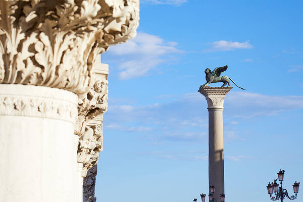 Saint Mark winged lion statue on column, symbol of Venice with blue sky and white capital 