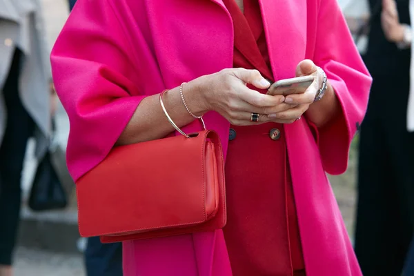 在2017年9月21日于米兰举行的米兰时装周街头时装秀之前，一位身穿红色皮包和迷幻粉红外套的女士正在看智能手机. — 图库照片