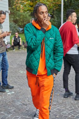 Versace defilesi öncesi yeşil Supreme ceketli ve turuncu spor kıyafeti giyen adam, Milano Moda Haftası sokak stili 22 Eylül 2017'de Milano'da.
