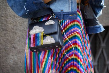 Woman with rainbow colors metallic pleated skirt with bag with cloud design with fringes before Ermanno Scervino fashion show, Milan Fashion Week street style on September 23, 2017 in Milan. clipart