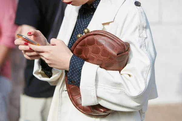 Mujer con bolso de reptil marrón y gabardina blanca mirando el teléfono inteligente antes del desfile de moda Gabriele Colangelo, Milan Fashion Week street style el 23 de septiembre de 2017 en Milán . —  Fotos de Stock