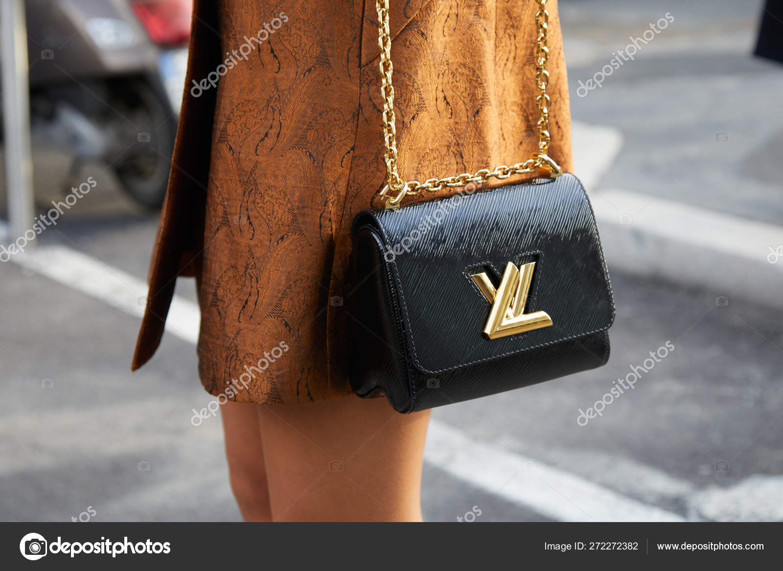 Mujer con bolso Louis Vuitton negro con logo dorado y chaqueta marrón antes  del desfile de