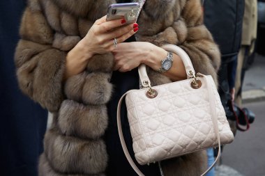 Albino Teodoro defilesinden önce bej rengi deri çantalı ve kahverengi kürklü bir kadın akıllı telefona bakıyor, Milan Moda Haftası 21 Şubat 2018 'de Milano' da.