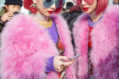 Pembe kürklü ve saçlı kadınlar Gucci moda defilesinden önce akıllı telefona bakıyorlar, Milan Moda Haftası 21 Şubat 2018 'de Milano' da.