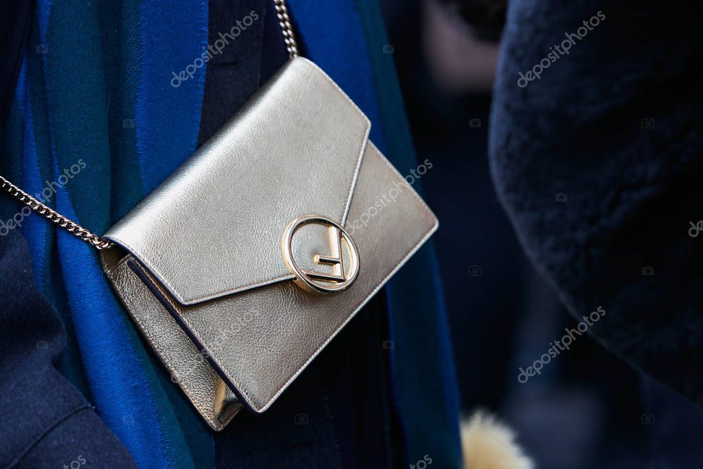 MILAN - FEBRUARY 22: Woman with leather metallic bag and blue scarf before Fendi fashion show, Milan Fashion Week street style on February 22, 2018 in Milan.