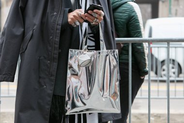 Fendi defilesinden önce akıllı telefona bakan gümüş metalik çantalı adam, Milano Moda Haftası sokak stili 15 Ocak 2018'de Milano'da.