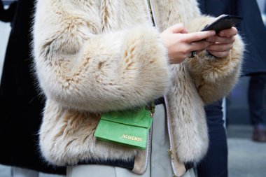 Yeşil Jacquemus çantalı ve bej kürklü bir kadın Frankie Morello moda defilesinden önce akıllı telefona bakıyordu. Milan Moda Haftası tarzı. 