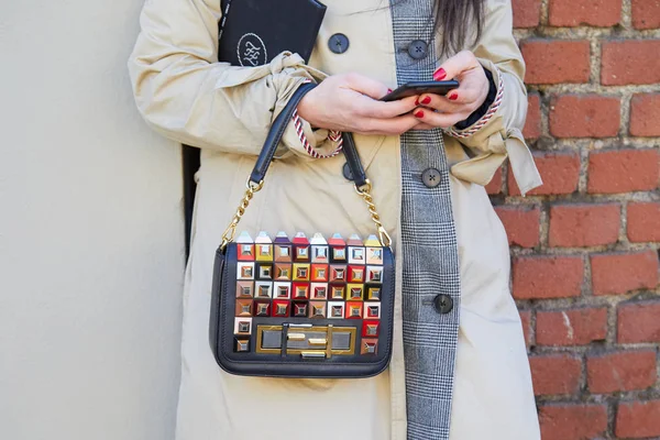 Kvinna med Fendi väska med färgglada dubbar tittar på smartphone innan Fendi modevisning, Milan Fashion Week street style — Stockfoto