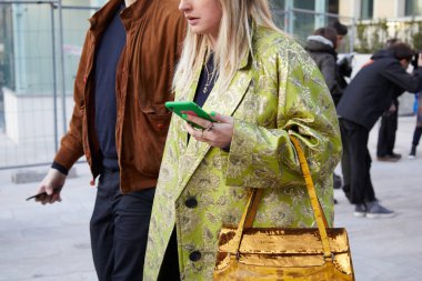 Neil Barrett moda defilesinden önce yeşil ve gümüş renkli siyah ceketli ve altın pullu bir kadın, Milan Moda Haftası tarzı. 