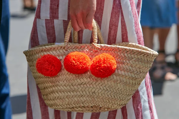 Woman with wiker bag with three orange pompom before Salvatore Ferragamo fashion show, Milan Fashion Week street style on June 18, 2017 in Milan. — Stock Photo, Image