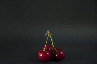 Üç Olgun kırmızı tatlı kiraz karanlık bir arka plan karşı izole. Koyu arka plan bir koyu gri masada özenle düzenlenmiş kiraz soyut ön görünüm. 