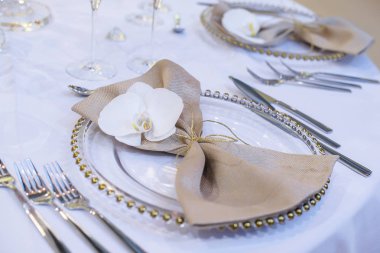 İyi yemek masa ayar featuring şeffaf levha, bej keten peçeteyle doğal orkide ve altın süslemeleri ve gümüş sırayla kullanın, bir resmi olay veya düğün konukları için hazır