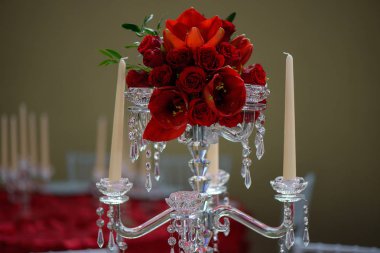 Horizontal close-up shot of a romantic formal table centerpiece, a beautiful crystal candelabra style candle holder with eight scalloped bobeche for candlesticks and a red tulips and roses bouquet