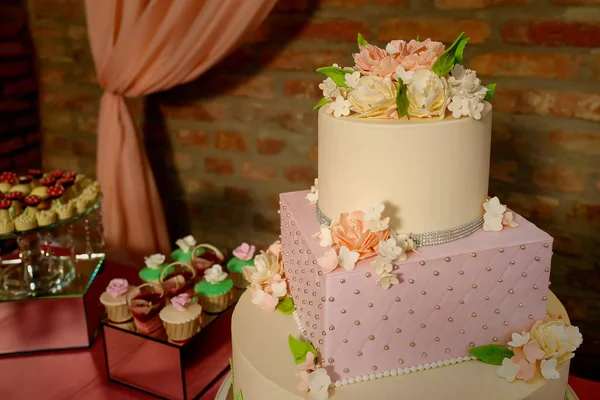 Large assortment of bite-sized cakes and a large three tiered cake embellished with velvet icing and sugar flowers, delicious dessert display at a wedding reception, a birthday party or a formal event