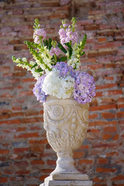 Minimalist white clay decorated flower pot with a spring bouquet featuring pastel hydrangeas, decorative element for a formal event or a wedding, with a terracotta color brick wall in the background