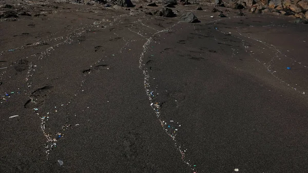 Plastic particles washed up by the waves on a beautiful black sand beach, damaging effect of human pollution, impacting the environment and affecting the marine ecosystem