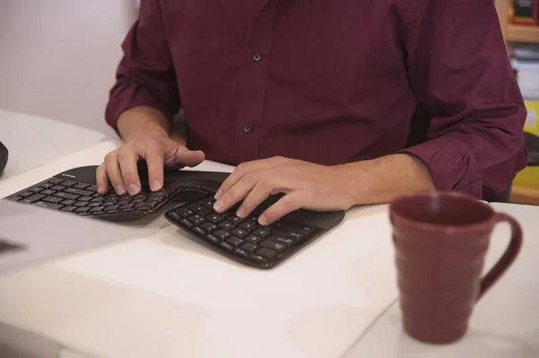 Erkek profesyonel bir masada oturan ergonomik bir klavye kullanarak. Atış tipik bir adamın, bir ofis veya bir çalışma ortamı, Bordo renkli gömlek eşleşen kahve ile belirlenmiş kırpılmış