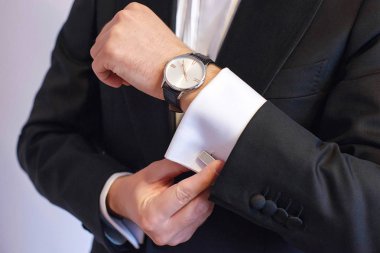 Sprezzatura ve zerafet onun kol düğmesi işareti sabitleme Genç beyaz beyaz erkek siyah kravat, yakın çekim shot. Damat, sofistike işadamı ya da bin yıllık erkek model hazırlanıyor.