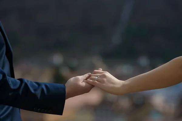 Heterosexual Caucasian couple holding hands with visible engagement and wedding rings, with a blurred, out-of-focus background, concept for a couple in love, marriage, togetherness and commitment