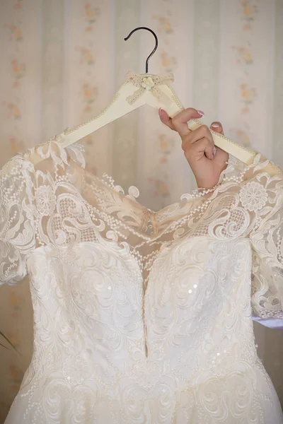 Woman hand holding an embroidered ivory white dress on a hanger featuring a sweetheart top, an elegant beige tulle lining and white sequins, elegant accessory for the bride to wear at the wedding day