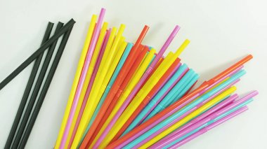 Çok renkli plastik içme pipetleri ve birkaç siyah kağıt içme pipetleri nötr bir yüzeye yayılmış, tek kullanımlık tek kullanımlık esnek pipetler, plastik kirliliğe ve alternatif kağıt çözümlerine neden
