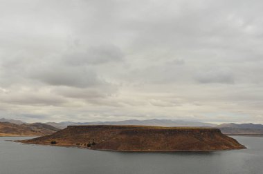 Dramatic and solitary landscape of small mountainous island known as Isla Umayo on Laguna Umayo during a windy and cloudy morning, view from the burial grounds of Sillustani, in the Puno region, Peru