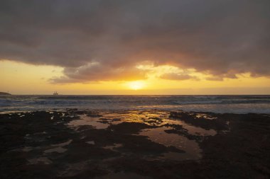 El Medano, Tenerife, Kanarya Adaları, İspanya kireçtaşı kıyılarında canlı, altın gündoğumu. Sakin suları ve uzakta bir siluet petrol kulesi ile Atlantik üzerinde mellow ışık gündoğumu.
