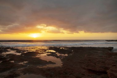 Görkemli gündoğumu El Medano tatil, Tenerife, Kanarya Adaları, İspanya, bulutlu gökyüzü ve altın pus ışığı ile canlı deniz manzarası kireçtaşı kıyılarında oluşan doğal su havuzları yansıyan