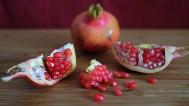 Bir bütün ve bir açık nar veya Kırmızı kümeleri ifşa Punica granatum meyve, sulu tohumlar, beyaz lifli arils ve kalın, mumlu kabuğu bordo bir arka plan ile ahşap bir tahta üzerinde istirahat