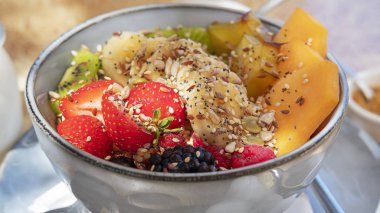 Lezzetli ve sağlıklı kahvaltı seçeneği, çilek, muz, kivi, yıldız meyvesi ve papaya, yulaf, besleyici fındık ve çekirdekli, süt veya yoğurt ve kahverengi şeker içeren tahıl ve meyve kasesi